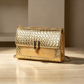 Sac doré rectangulaire avec rabat à relief géométrique et bandoulière chaîne sur un décor beige.