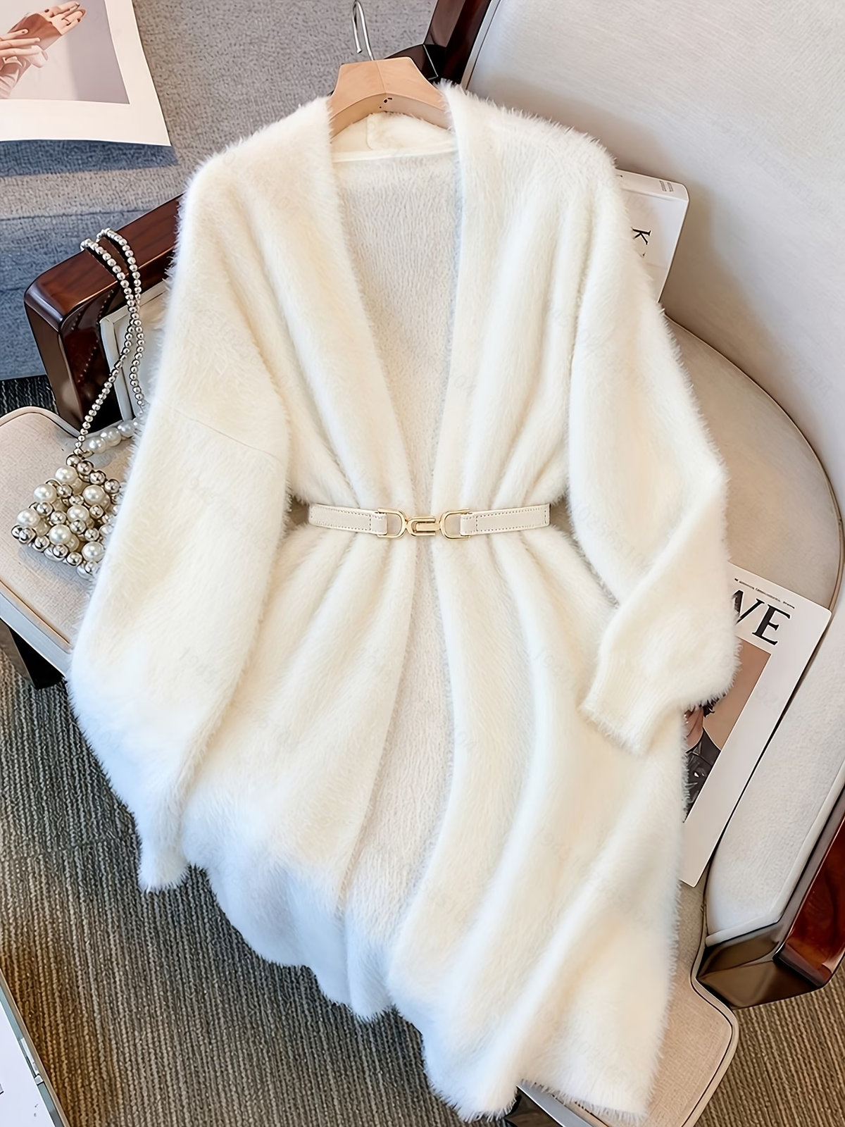 Gilet ivoire d’aspect duveteux présenté avec une fine ceinture claire à détail doré