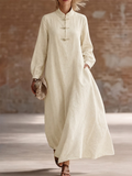 Robe longue ivoire à col montant, manches longues et attaches décoratives, portée par une femme